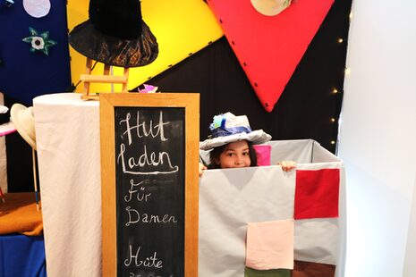Bunte Theaterkulisse, ein Kinderkopf mit Hut schaut aus einem Karton heraus