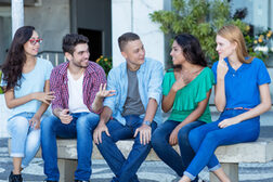 Eine Gruppe junger Menschen sitzt nebeneinander auf einer Bank und unterhält sich