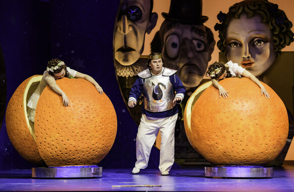 Zwei Frauen stehen in überdimensionierten Orangen, in der Mitte steht ein Mann