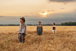 Drei Personen stehen in einem Getreidefeld